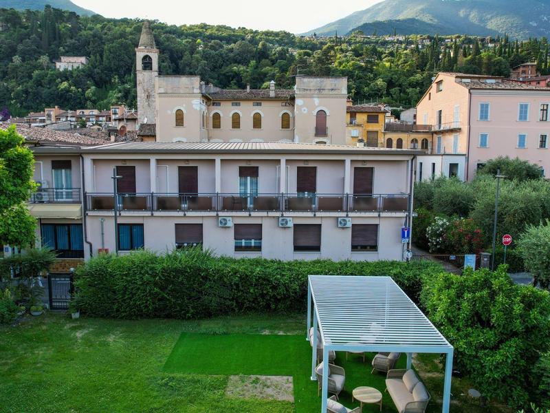 Vista di un giardino con prato verde e pergola davanti a una casa con montagne sullo sfondo.