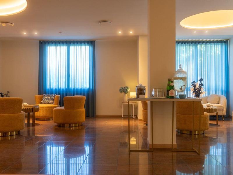 Accogliente area lounge dell'hotel con poltrone arancioni, tavoli e luce delle tende blu.