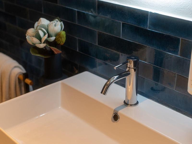 Lavandino bianco moderno con rubinetto monocomando e dispenser di sapone davanti a parete piastrellata nera.