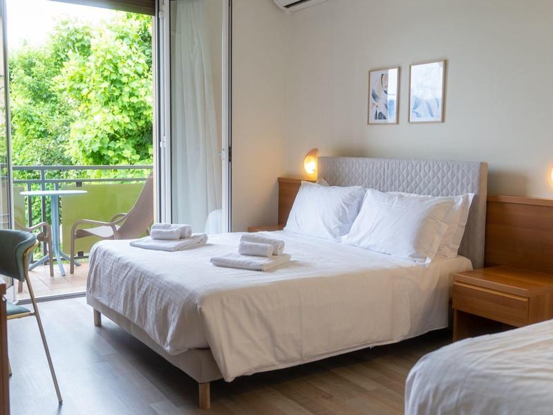 Camera d'hotel luminosa con due letti, balcone e vista rilassante sul verde.