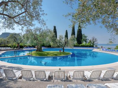 Piscina rotonda con isola al centro e lettini intorno, in un paesaggio mediterraneo.
