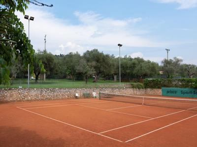 Campo da tennis in terra rossa con alberi verdi e cielo grigio-azzurro sullo sfondo.