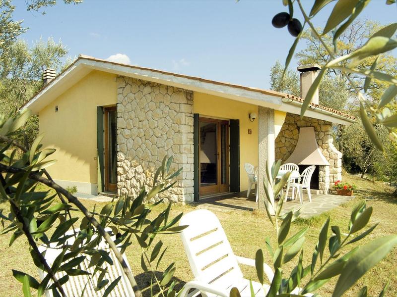Piccola casa vacanze con muro in pietra e terrazza in un giardino soleggiato.
