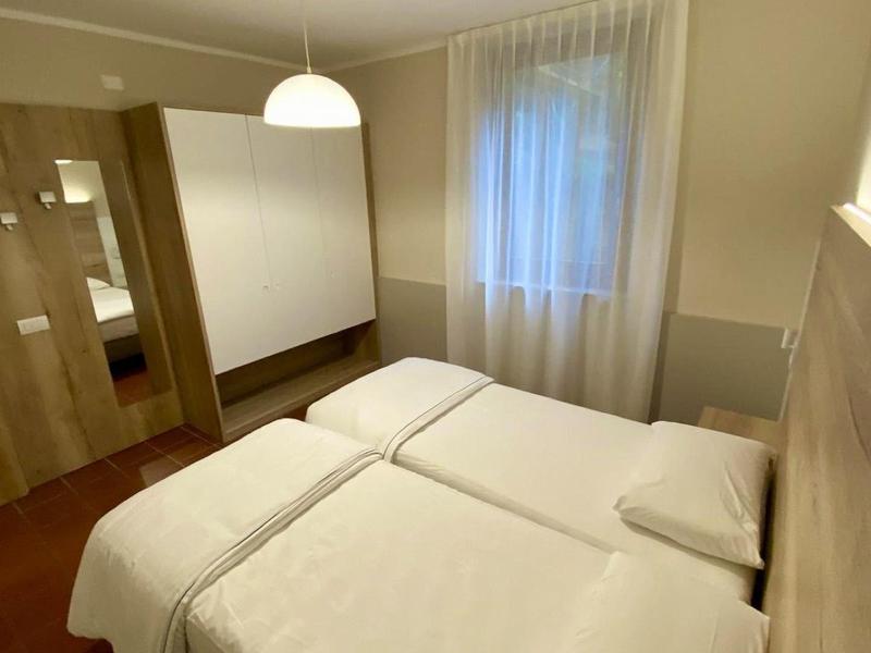 Camera d'hotel luminosa con due letti singoli, biancheria bianca e tenda alla finestra.