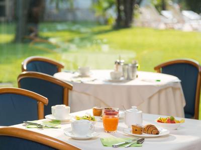 Stůl s příbory, pečivem a nápoji před stolem s bílým ubrusem venku.