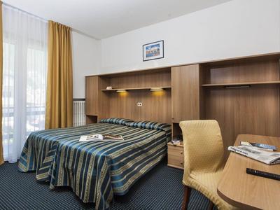 Ein einfaches Hotelzimmer mit zwei Betten, Holzmöbeln, gelben Vorhängen und Teppichboden.