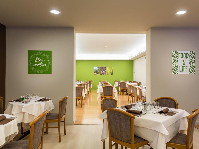 Restaurant mit rechteckigen Holztischen, weißen Tischdecken und grün dekorierten Wänden.