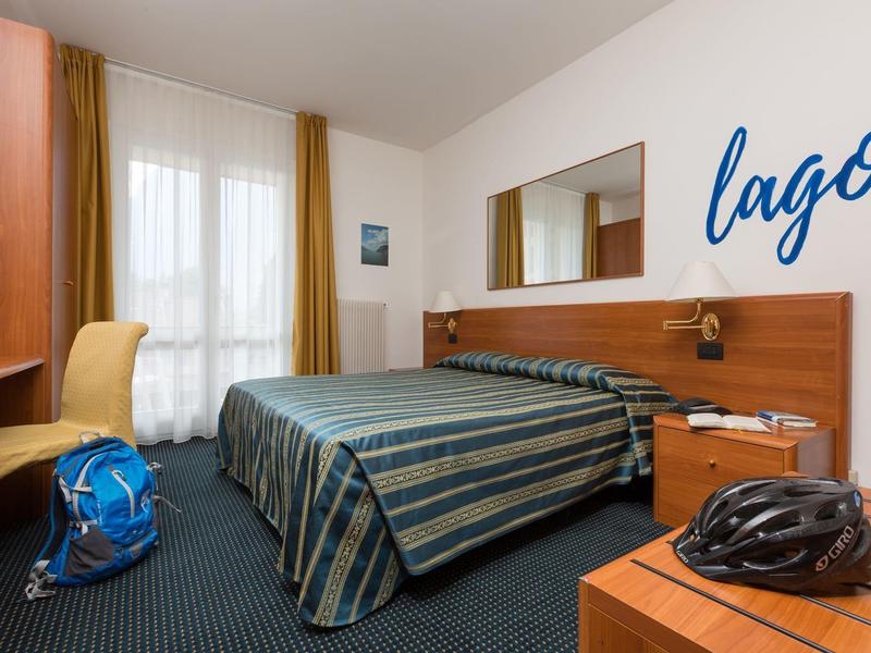 Ein einfach eingerichtetes Hotelzimmer mit Doppelbett, blau gestreifter Bettdecke und gelben Vorhängen.