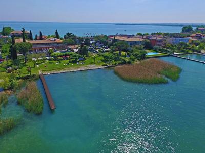Klares Wasser, grüne Ufer mit Pflanzen, Gebäude und blauer Himmel über ruhigem See.