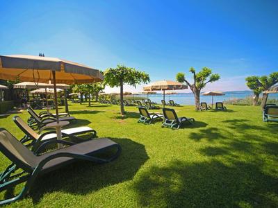 Tumbonas y sombrillas sobre césped verde con vista al mar bajo cielo azul claro.