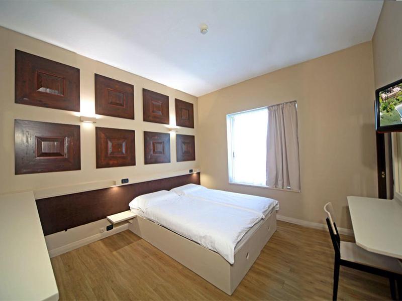 Kleines helles Schlafzimmer mit großem Doppelbett, Holzfußboden und TV an der Wand.