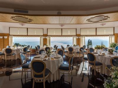 Sala da pranzo elegante con tavoli rotondi apparecchiati e vista sul mare.