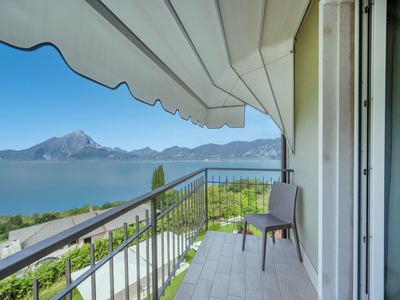 Balcone con sedia, tenda da sole e vista su lago e montagne in giornata limpida.
