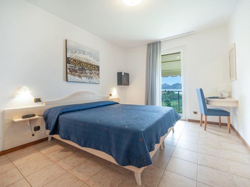 Camera d'hotel luminosa con letto matrimoniale, copriletto blu, scrivania e vista sul paesaggio verde.