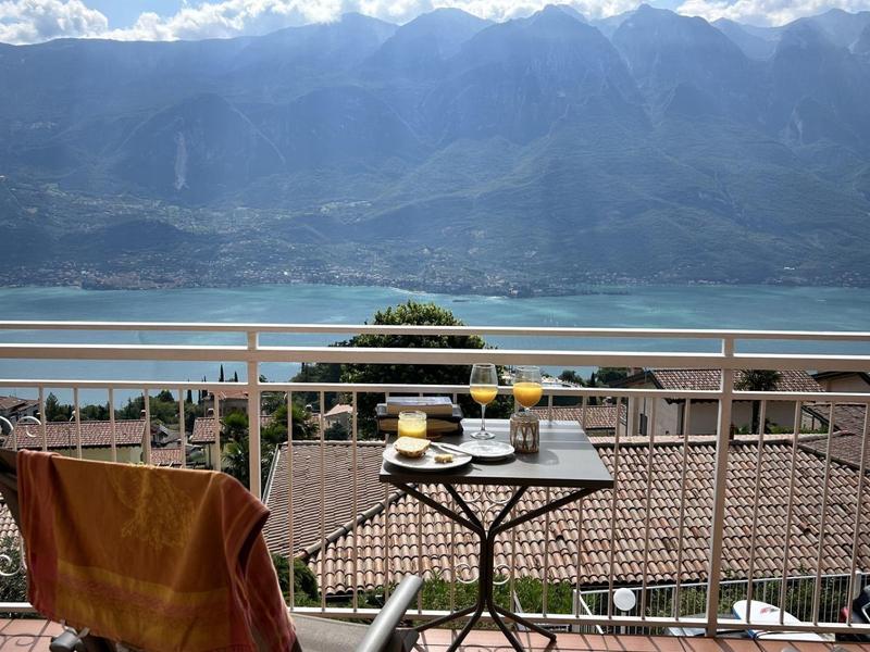 Balcone con sedie, tavolo e vista sul lago e le montagne sotto un cielo blu.