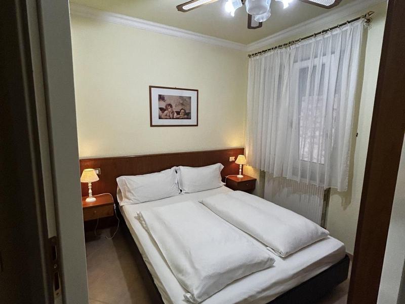 Camera d'hotel accogliente con letto matrimoniale, comodini, ventilatore a soffitto e finestra con tende.