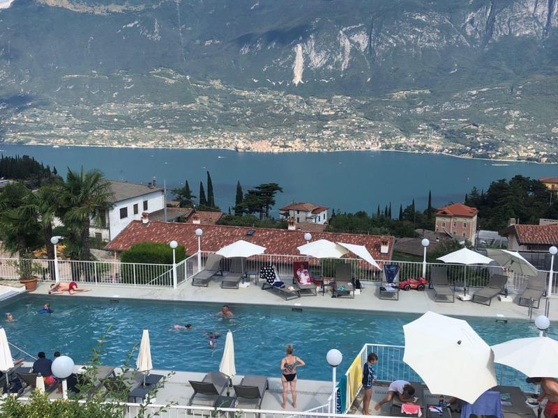 Vista di una piscina con ombrelloni e montagne sullo sfondo vicino al lago.