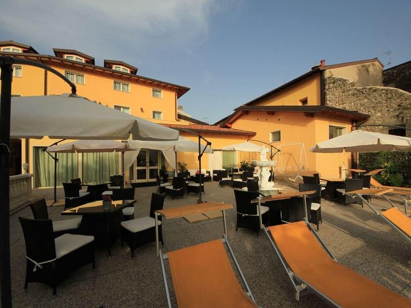 Espace extérieur d'un hôtel avec chaises longues et tables sous parasols devant des bâtiments jaunes.