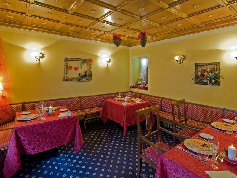 Salle à manger conviviale avec murs en bois, nappes rouges, tapis bleu et tables dressées.