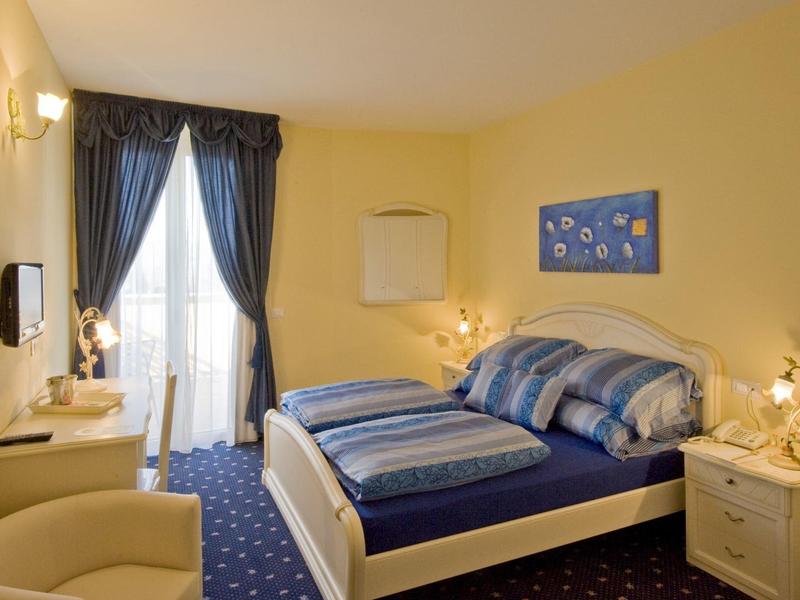 Chambre d'hôtel confortable avec lit double, tapis et rideaux bleus, murs jaunes et balcon.