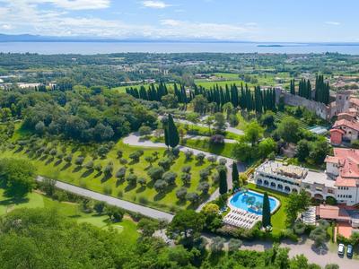 Luchtfoto van een hotel met zwembad, omgeven door groene velden dicht bij een groot water.