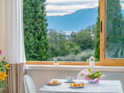 Una mesa de desayuno puesta junto a una ventana abierta con vista a árboles verdes y montañas.