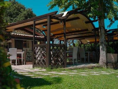 Open paviljoen met tafels en stoelen in een schaduwrijke tuin bij zonlicht.