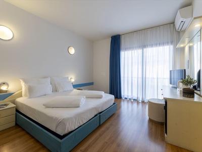 Modern eingerichtetes Hotelzimmer mit Doppelbett, Schreibtisch und großem Fenster mit Vorhängen.