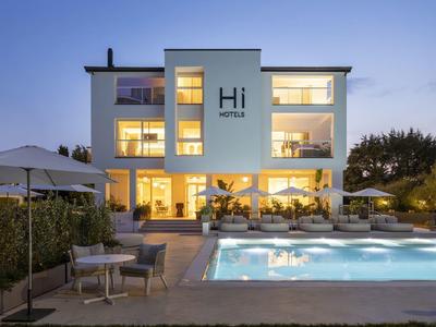 Hotel moderno de tres pisos con piscina iluminada y terrazas al anochecer.