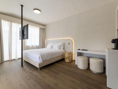 Habitación de hotel luminosa con cama doble, televisor en el techo y escritorio con taburetes.