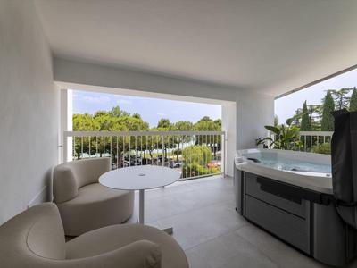 Balcón con dos sillones, mesa pequeña y jacuzzi con vistas al paisaje verde.