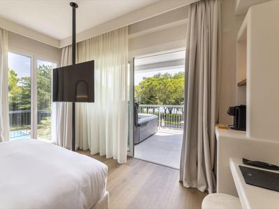 Habitación de hotel moderna con cama, TV, cortinas y acceso a terraza con zona de estar.