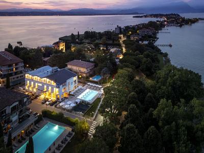 Abendliche Luftaufnahme eines beleuchteten Hotels mit Pool am Seeufer und bewaldeter Umgebung.
