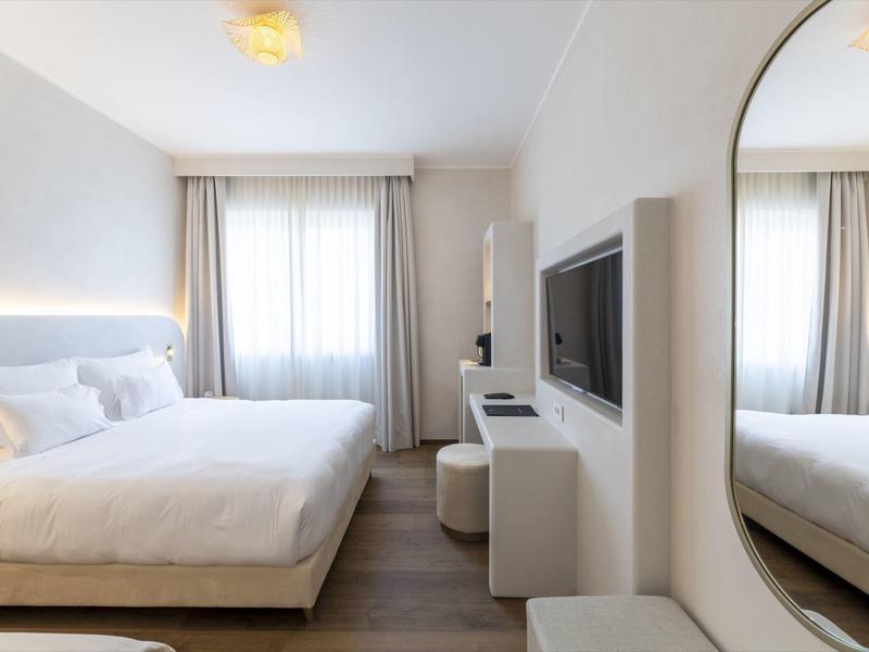 Habitación de hotel moderna con cama grande, TV y espejo en la pared.