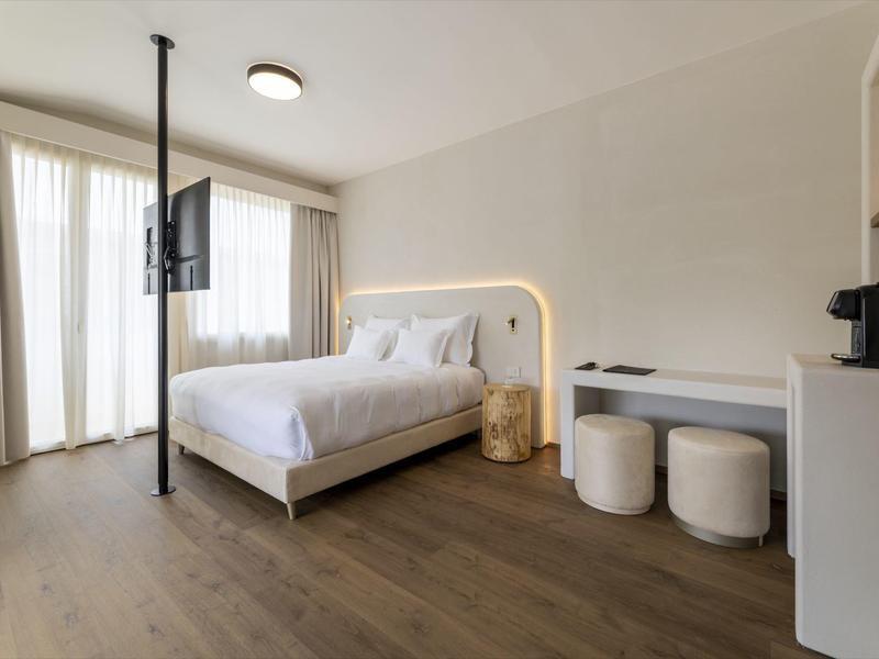 Habitación de hotel luminosa con cama doble, televisor en el techo y escritorio con taburetes.