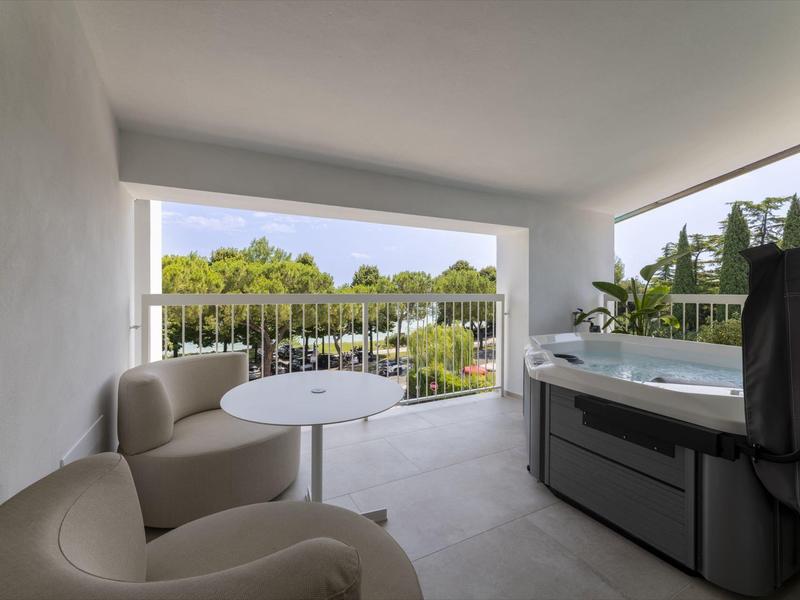 Balcón con dos sillones, mesa pequeña y jacuzzi con vistas al paisaje verde.