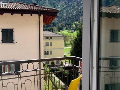 Balkon mit gelbem Stuhl und Blick auf Berge und Gebäude bei klarem Himmel.