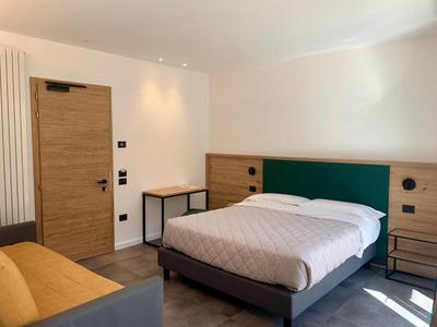 Modernes Hotelzimmer mit Doppelbett, grünem Kopfteil, Holztür und gelbem Sofa