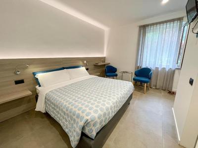 Modernes Hotelzimmer mit großem Doppelbett, zwei blauen Sesseln und Fenster mit Vorhang.