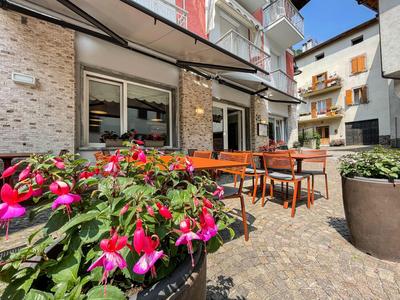 Außenterrasse eines Hotels mit Tischen, Stühlen und blühenden Pflanzen bei sonnigem Wetter.