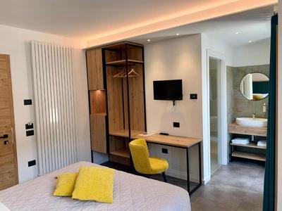 Modernes Hotelzimmer mit Schreibtisch, gelbem Stuhl und Bad im Hintergrund.