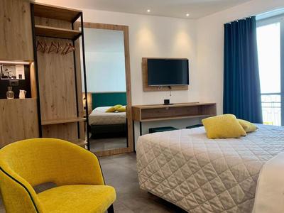 Modernes Hotelzimmer mit gelbem Sessel, offenem Kleiderschrank, großem Spiegel und TV an der Wand.