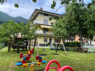Ein Garten mit Spielplatz, Schaukeln und Sitzgelegenheiten vor einem dreistöckigen Haus.