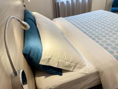 Ein gemütlich gemachtes Bett mit weißen Bettlaken und blauen Kissen neben einem Leselicht.