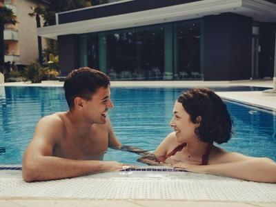 Zwei Personen entspannen im Pool eines Hotels und lachen miteinander.