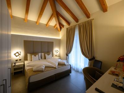 Modernes Hotelzimmer mit Holzbalkendecke, großem Bett, Vorhängen und gemütlicher Beleuchtung.
