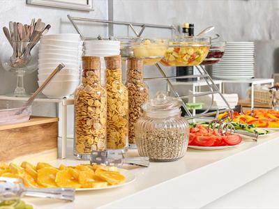 Bufet s cereáliemi, čerstvým ovocným salátem, plátky kdouloně a různými talíři zeleniny v moderním hotelu.