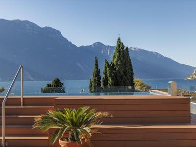 Holzterrasse mit Blumen, Blick auf Berge und See bei klarem Himmel.
