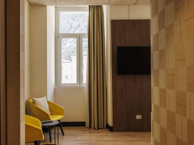 Modern eingerichtetes Hotelzimmer mit zwei gelben Sesseln und Fenster mit langem Vorhang.