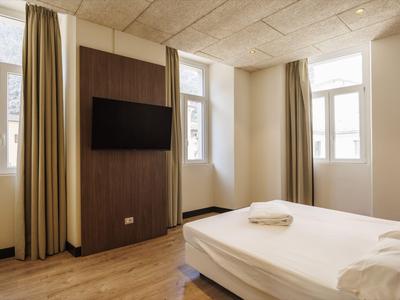 Hell eingerichtetes Hotelzimmer mit Doppelbett, Fernseher und großen Fenstern.
